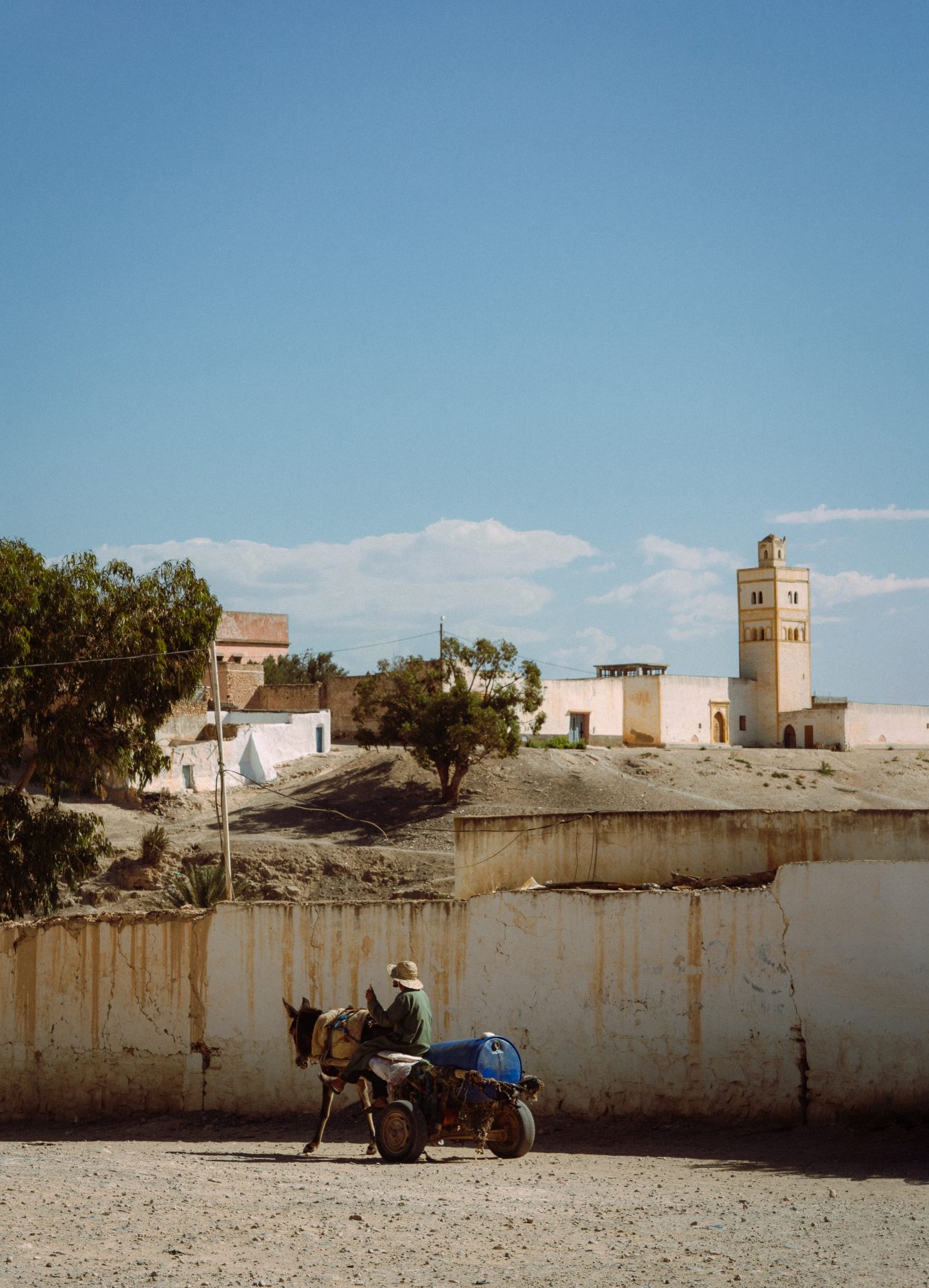 Un homme marocain sur une charrette tirée par un cheval. Un mur l'empêche d'admirer la vue décorée d'une mosquée