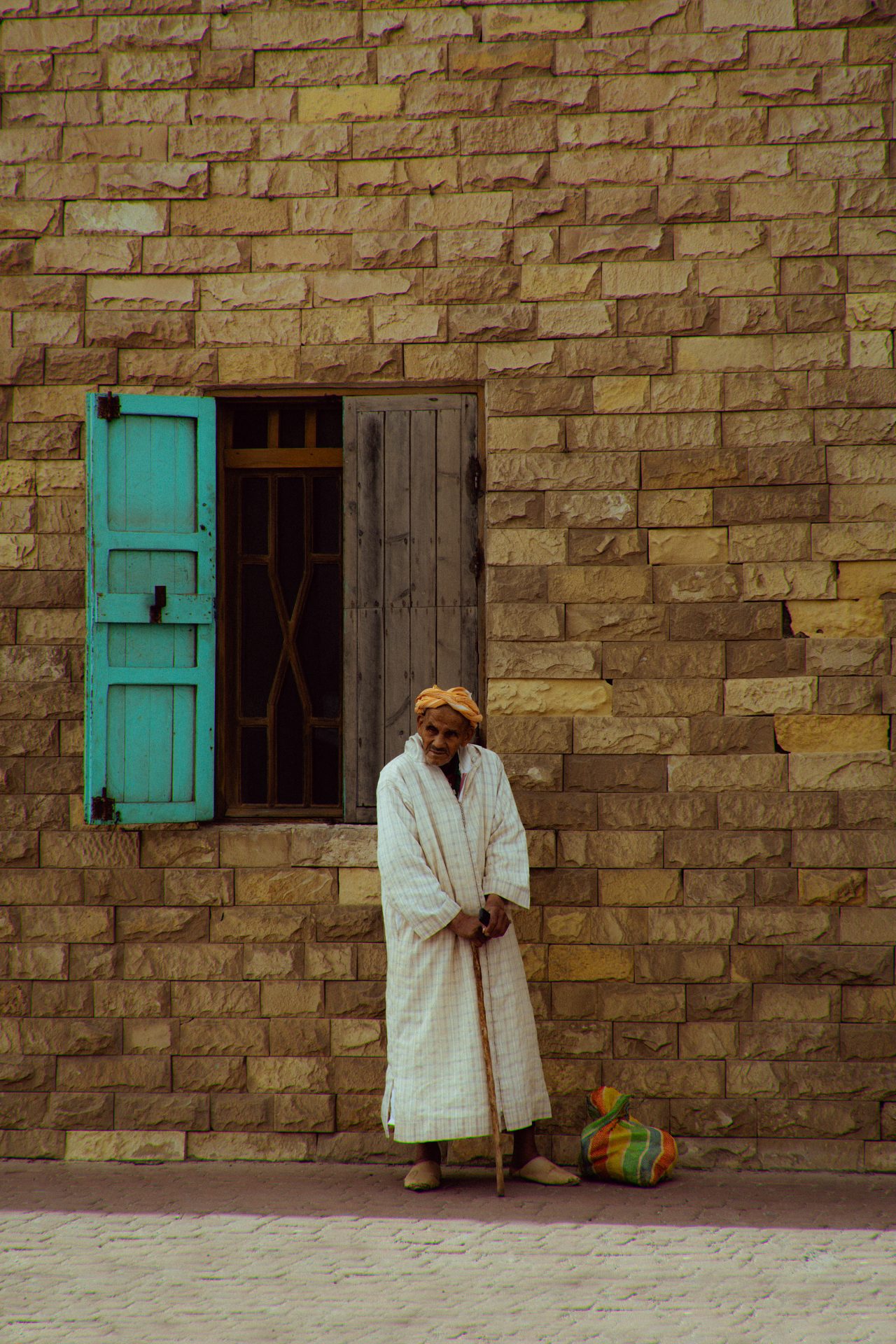 Un homme habillée d'une robe blanche et d'un turban jaune se tient sur sa canne.