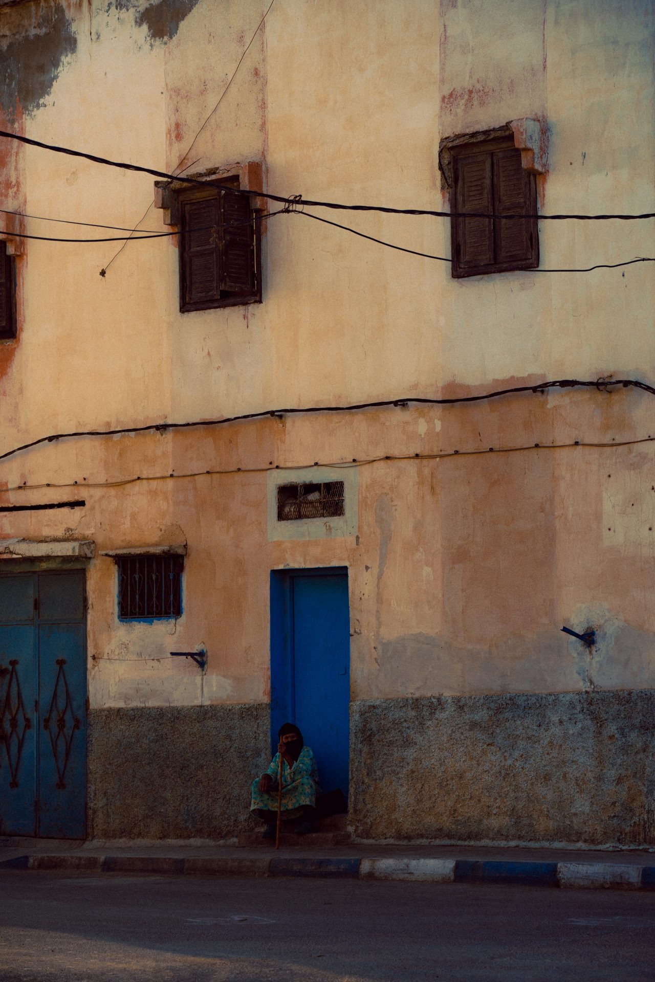 Une personne est assise avec sa canne devant une porte bleue près d'Agadir