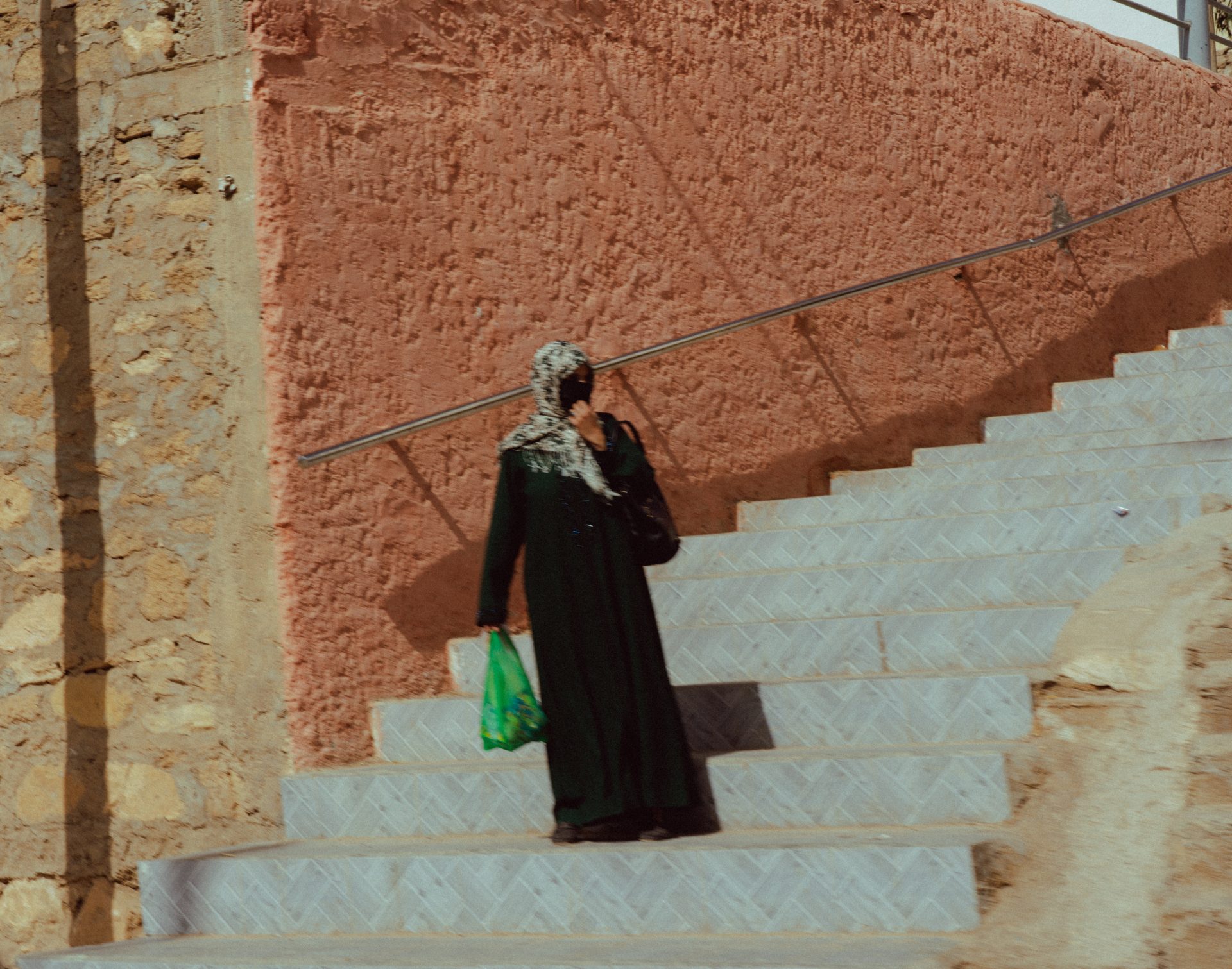 Une femme voilée descend des marches, un sac platique vert à la main.