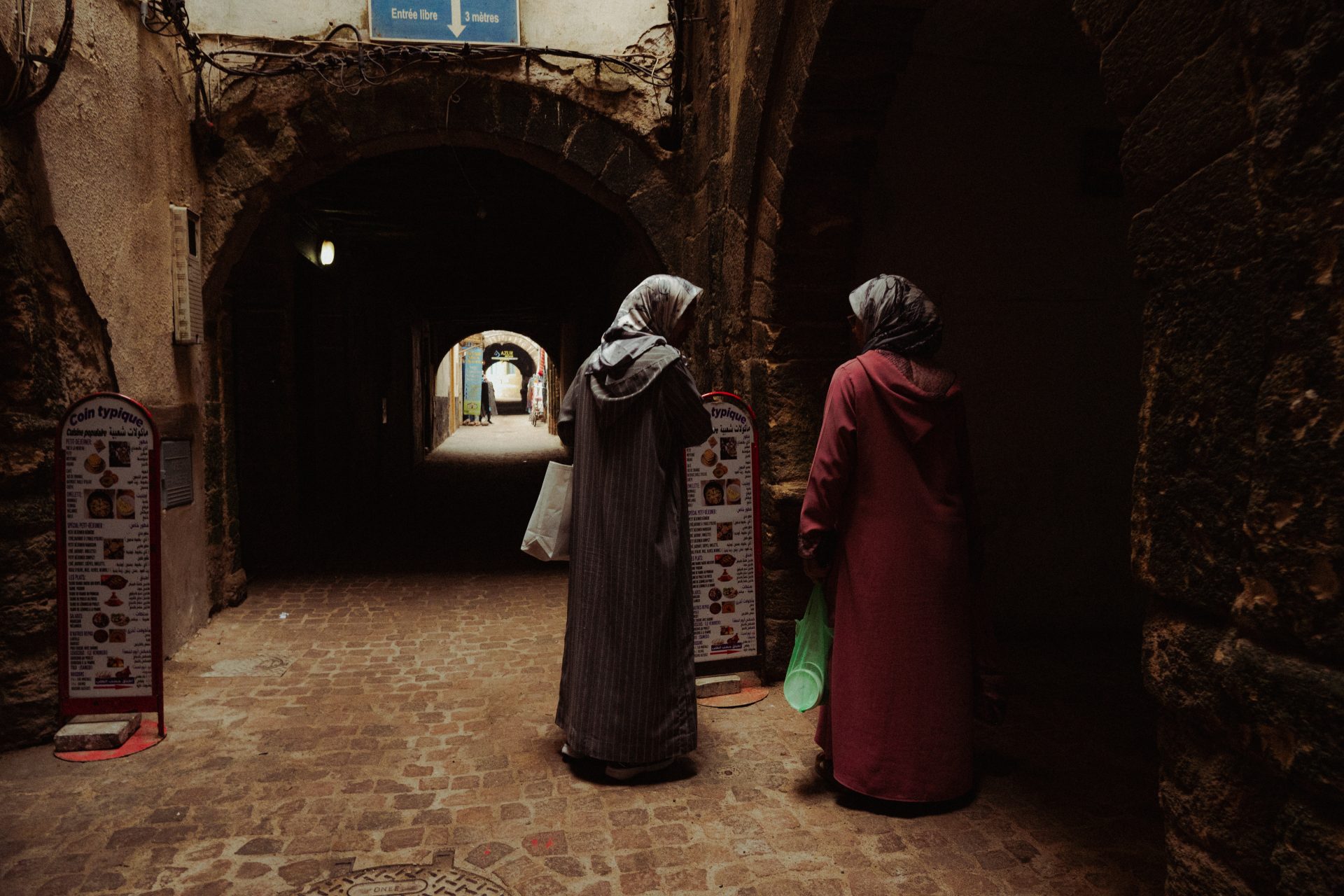 Deux femmes voilées échangent dans une ruelle sombre d'Essaouira.